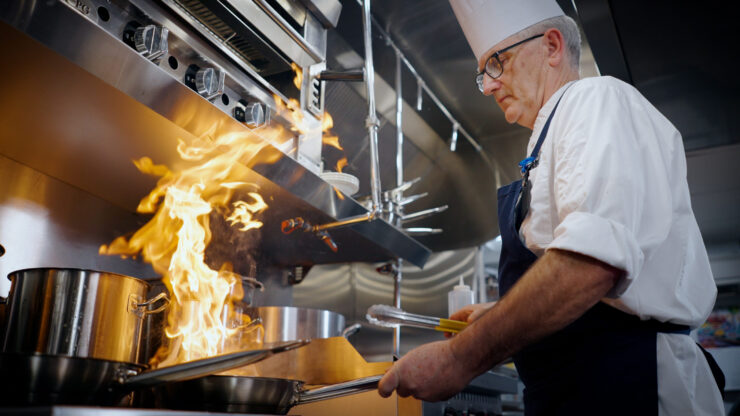 A skilled chef passionately creates delicious meals, showcasing vibrant flames in a warm, inviting kitchen.