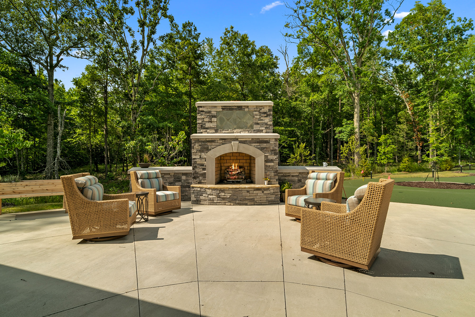 A welcoming outdoor space features comfortable seating around a charming stone fireplace, surrounded by nature.