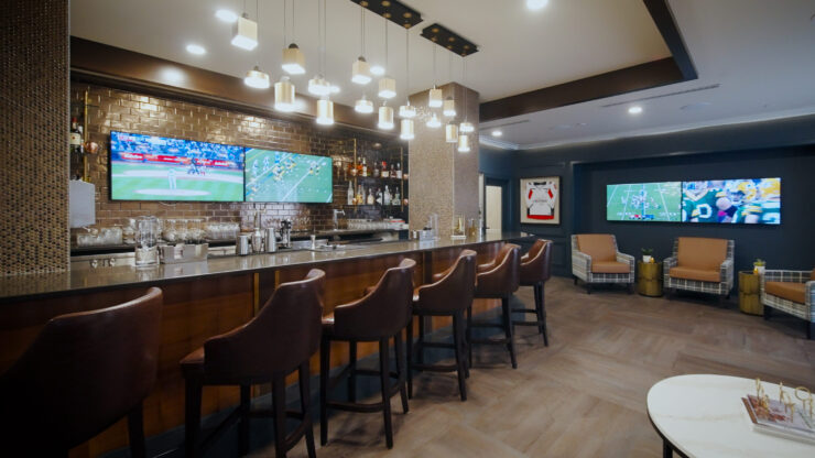 A welcoming lounge features a stylish bar, comfortable seating, and screens displaying lively sports, fostering community and relaxation.