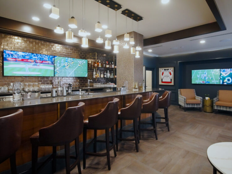 A welcoming lounge features a stylish bar, comfortable seating, and screens displaying lively sports, fostering community and relaxation.