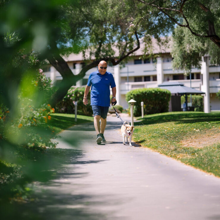 A resident enjoys a leisurely stroll with a dog, surrounded by lush greenery and a welcoming atmosphere.