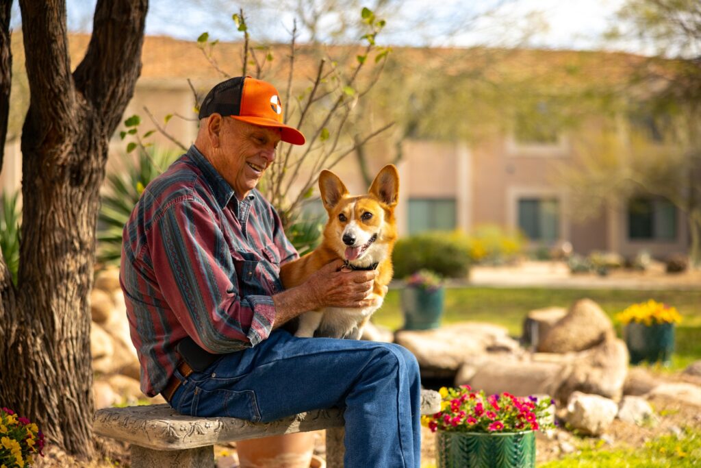 A joyful moment shared between a resident and a playful corgi in a vibrant garden setting.