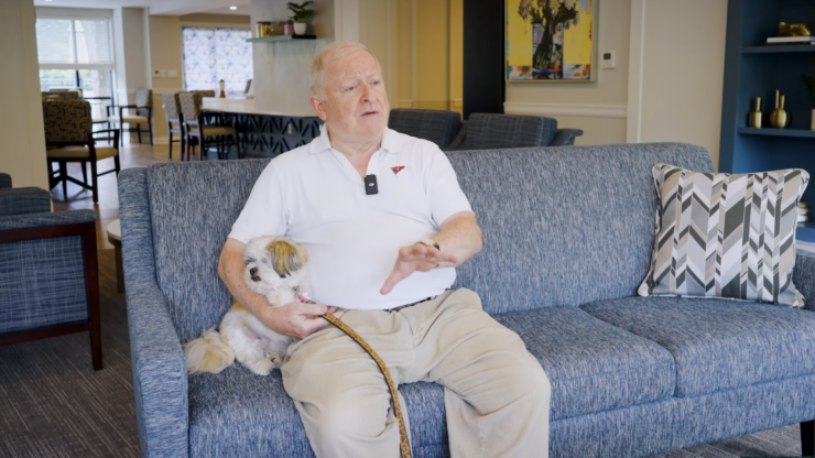 A resident shares a moment on a comfortable couch with a small dog, highlighting community warmth and companionship.