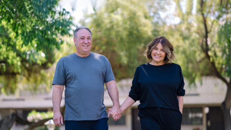 A cheerful couple strolls hand-in-hand through a vibrant, green garden, embodying warmth and connection.