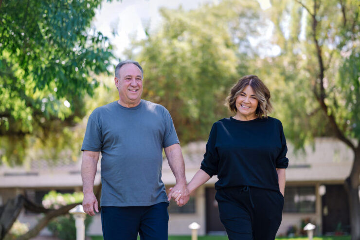 A cheerful couple strolls hand-in-hand through a vibrant, green garden, embodying warmth and connection.