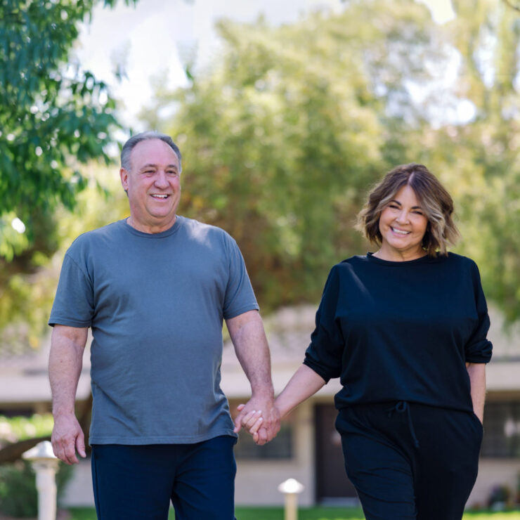 A cheerful couple strolls hand-in-hand through a vibrant, green garden, embodying warmth and connection.
