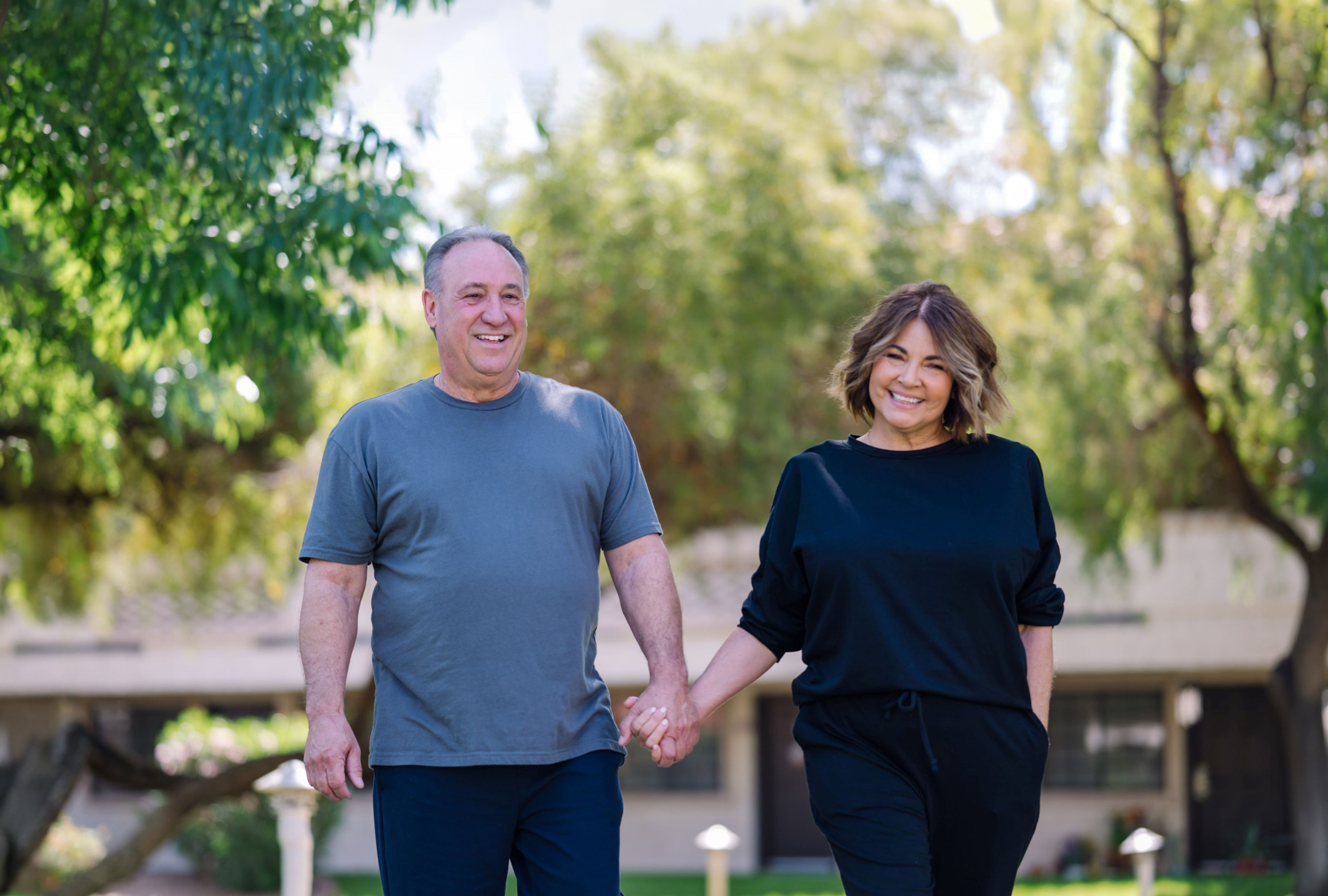 A cheerful couple strolls hand-in-hand through a vibrant, green garden, embodying warmth and connection.