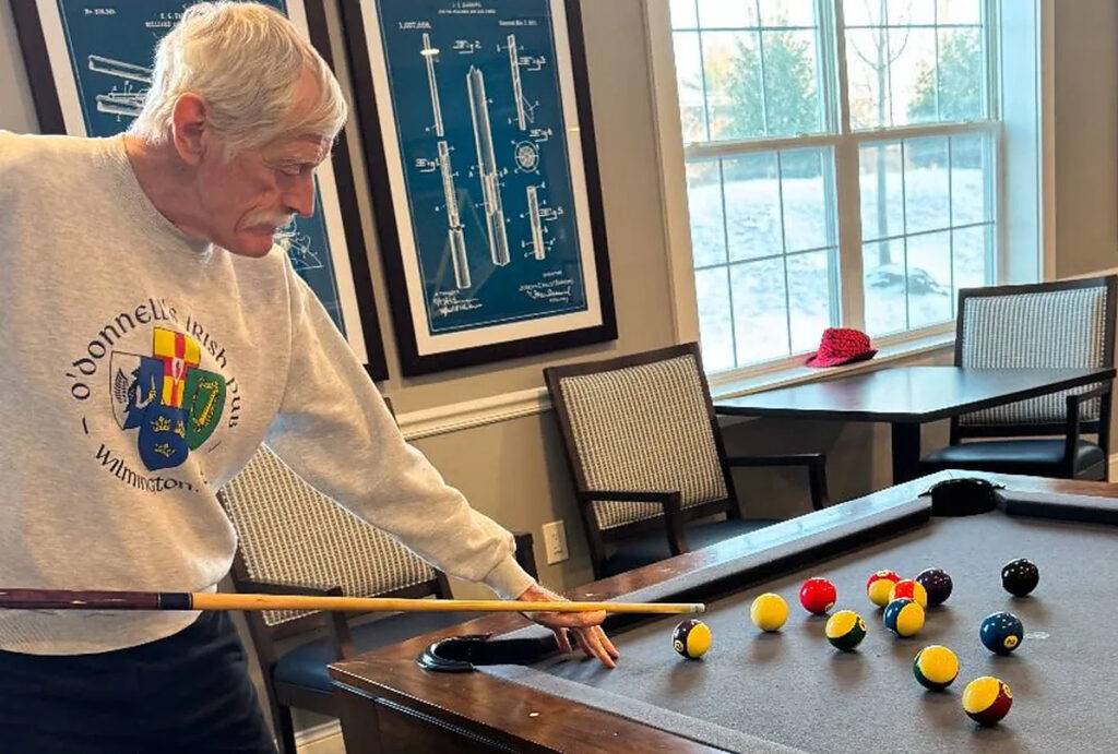 Senior man focused on a friendly game of pool in a bright, inviting community room.