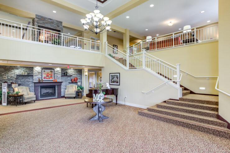 Bright and inviting retirement home lobby with seating, fireplace, and elegant staircase.