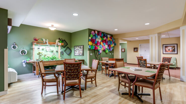 Bright community room with tables, chairs, colorful décor, and plants for relaxation and socializing.