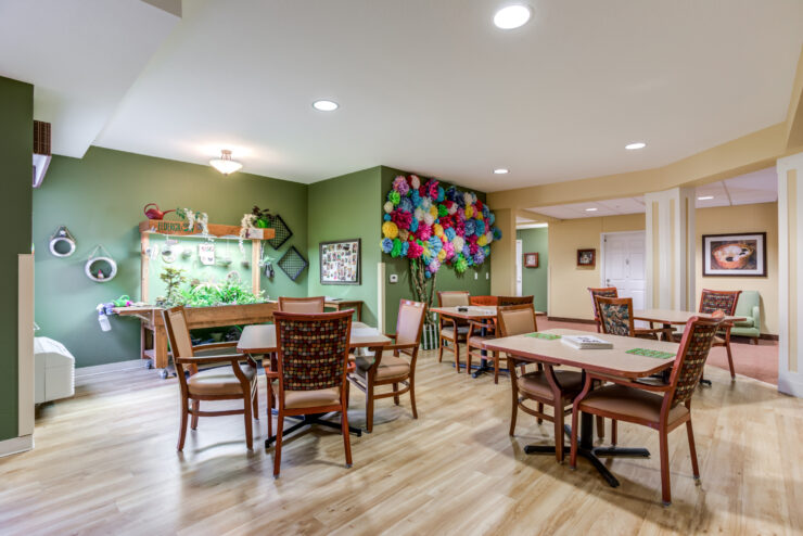 Bright community room with tables, chairs, colorful décor, and plants for relaxation and socializing.