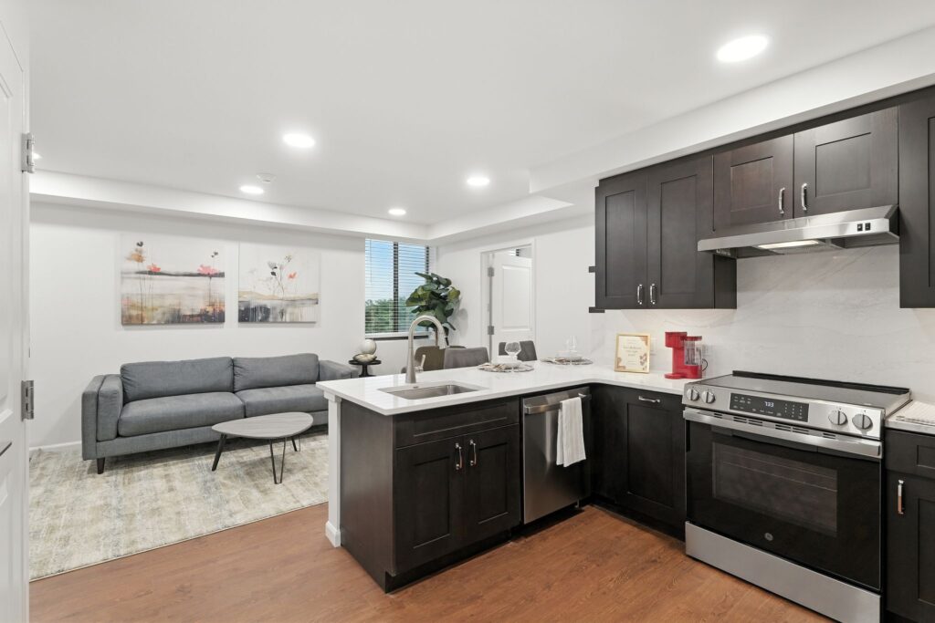 Modern kitchen and living area with dark wood cabinets, comfortable seating, and natural light.