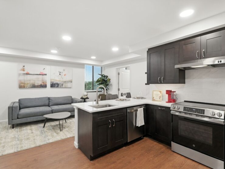 Modern kitchen and living area with dark wood cabinets, comfortable seating, and natural light.