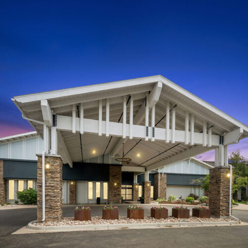 Welcoming entrance of a retirement home with warm lighting and landscaped surroundings at dusk.