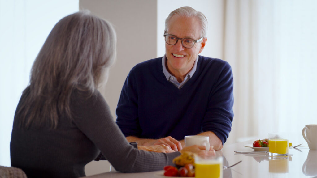 Two seniors enjoy a warm conversation over breakfast in a bright, inviting dining area.