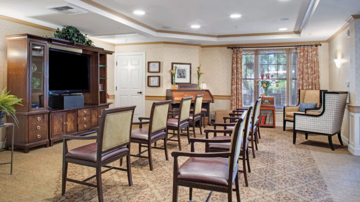 Well-lit activity room with arranged seating, a piano, and a large window overlooking greenery.