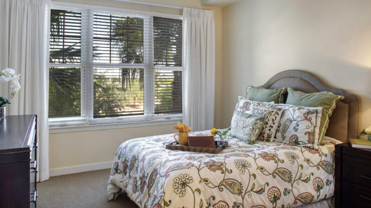 Sunlit bedroom with patterned bedding, soft pillows, and a tray with a book and cup.