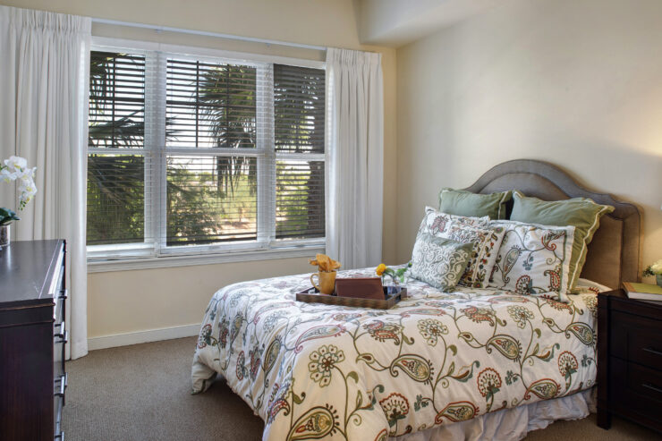 Sunlit bedroom with patterned bedding, soft pillows, and a tray with a book and cup.