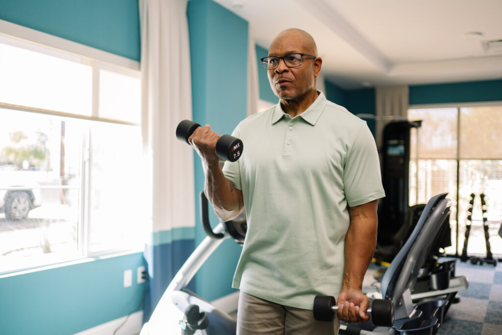 Senior man exercising with hand weights in a bright, welcoming fitness room.