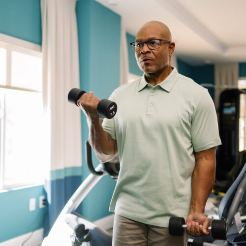 Senior man exercising with hand weights in a bright, welcoming fitness room.