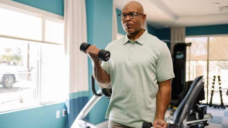 Senior man exercising with hand weights in a bright, welcoming fitness room.