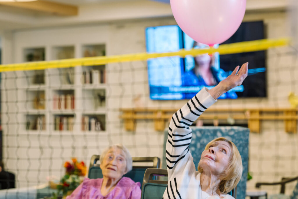 Residents engage joyfully in a lively balloon game, fostering connection and laughter in a warm community space.