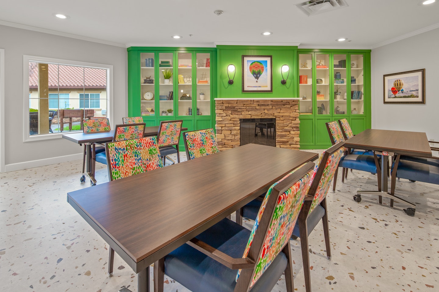 Bright and inviting activity room with colorful chairs and a warm stone fireplace in a community setting.