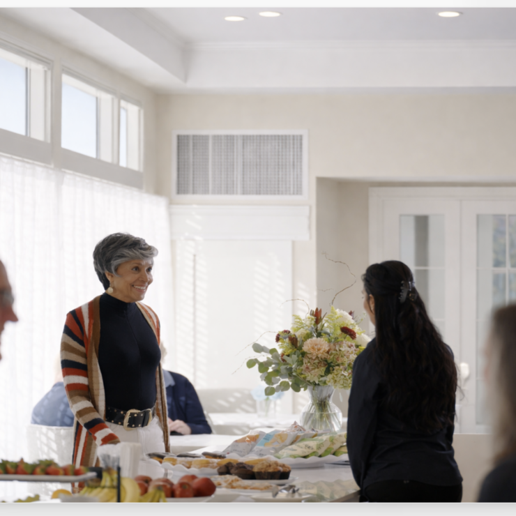 Residents and staff warmly engaging in conversation around a table with snacks and flowers.