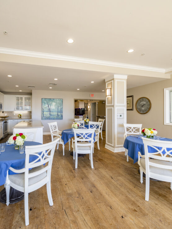 Bright dining area with blue tablecloths, fresh flowers, and comfortable seating for residents.