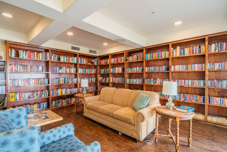 Inviting library lounge with plush seating, warm wood shelves, and abundant books for residents to enjoy.