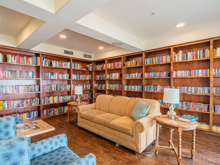 Inviting library lounge with plush seating, warm wood shelves, and abundant books for residents to enjoy.