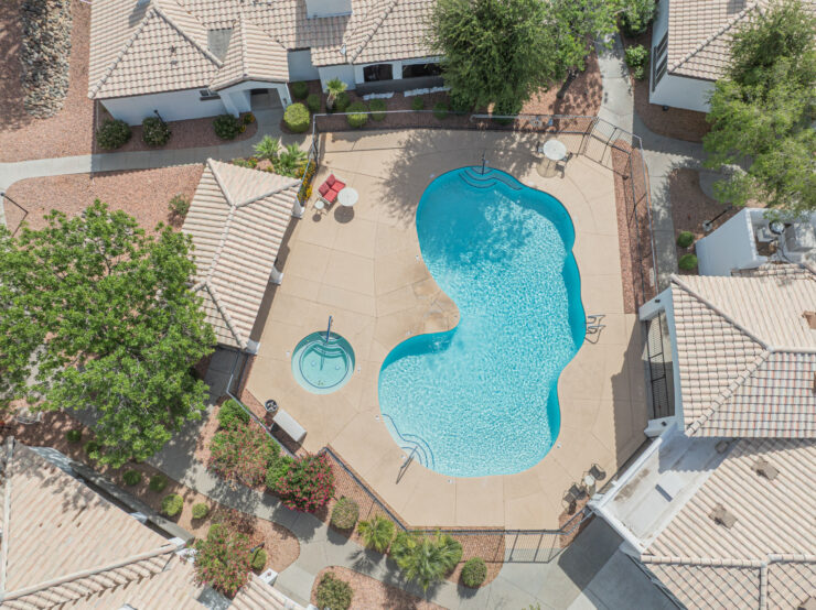 Sunlit swimming pool area surrounded by shaded seating and landscaped pathways in a serene community setting.