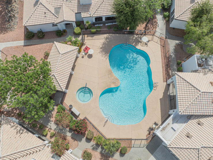 Sunlit swimming pool area surrounded by shaded seating and landscaped pathways in a serene community setting.