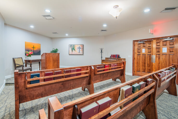Bright chapel with wooden pews, hymnals, piano, and warm welcoming decor for reflection and community.