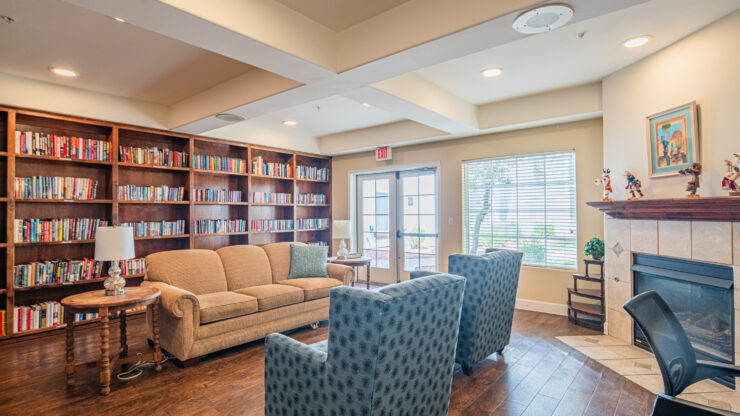 Inviting common room with bookshelves, comfortable seating, natural light, and a fireplace.