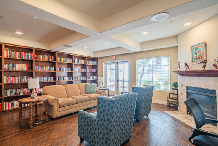 Inviting common room with bookshelves, comfortable seating, natural light, and a fireplace.