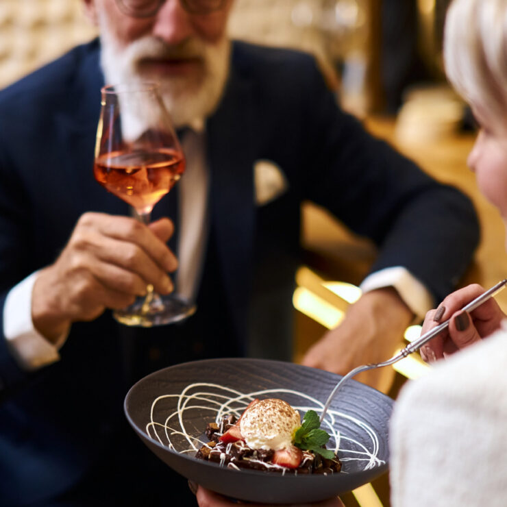 Elegant seniors enjoying dessert and wine together in a warm, inviting setting.