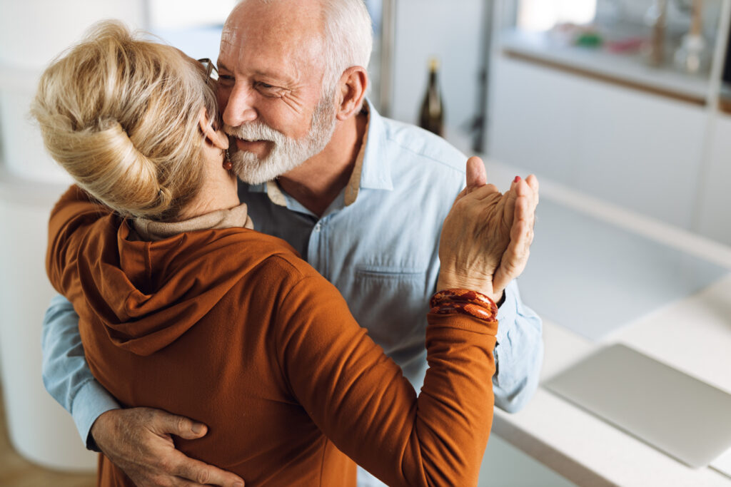 Elderly couple embracing and dancing gently in a warm, inviting home setting.