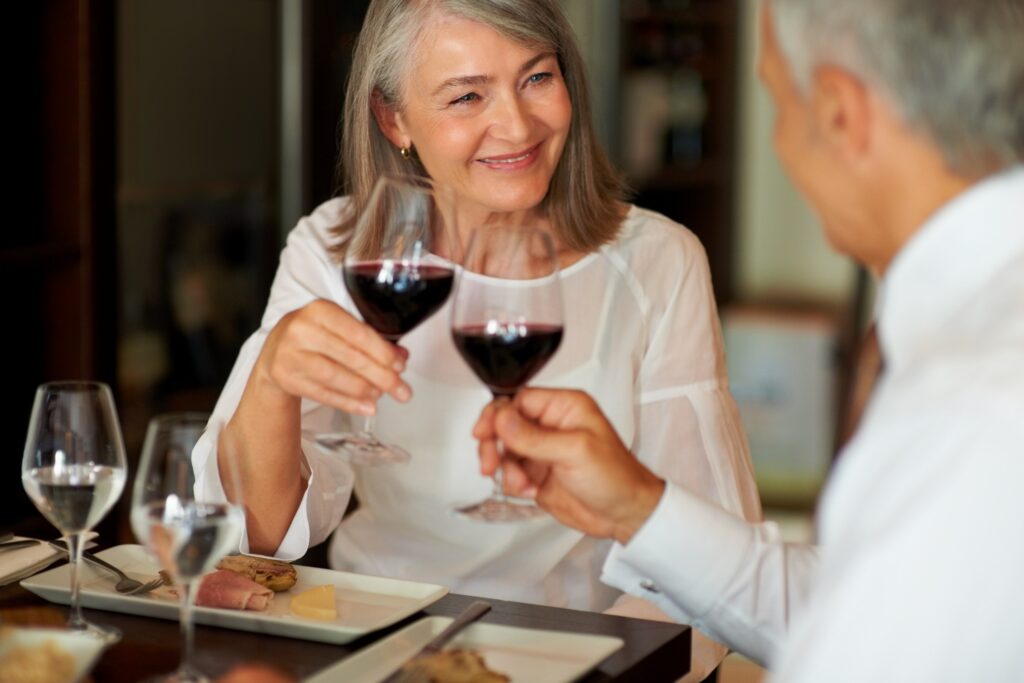 Two seniors sharing a joyful toast with red wine in a warm, inviting dining atmosphere.