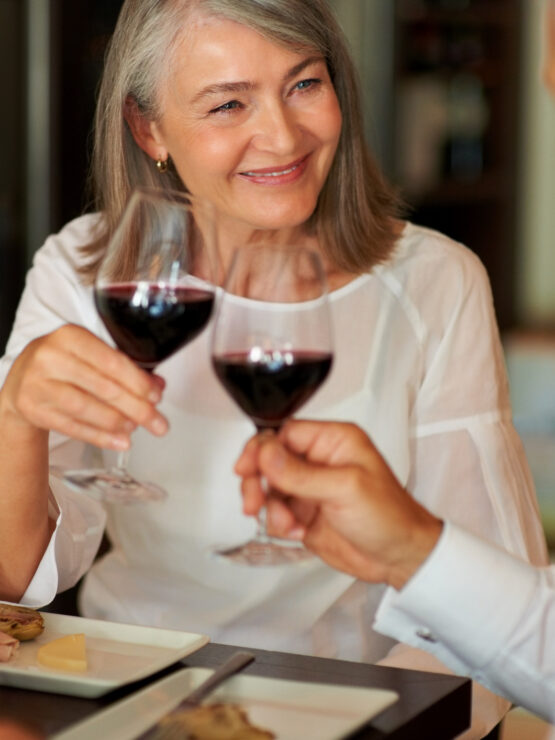 Two seniors sharing a joyful toast with red wine in a warm, inviting dining atmosphere.