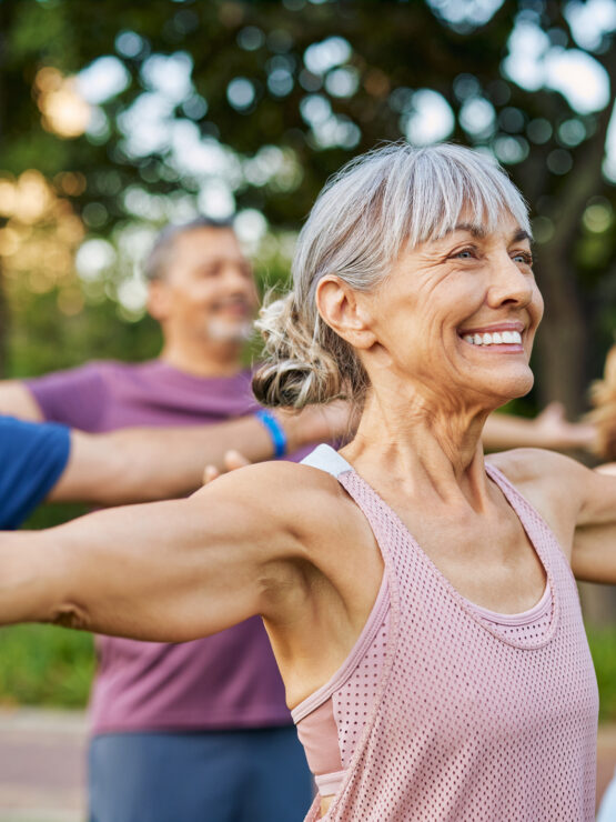 Active seniors enjoying a group exercise session outdoors in a peaceful, green park setting.