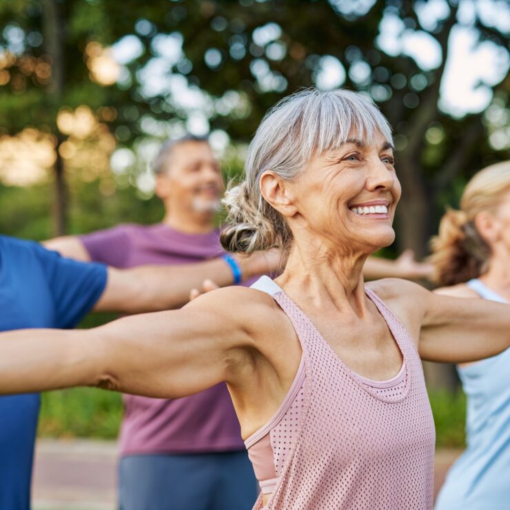 Active seniors enjoying a group exercise session outdoors in a peaceful, green park setting.