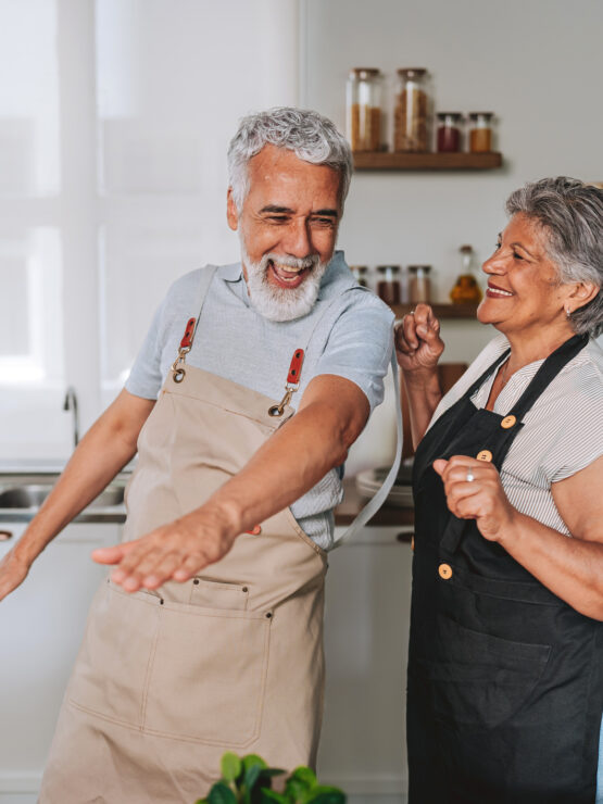 Senior couple wearing aprons joyfully dancing together in a bright, welcoming kitchen setting