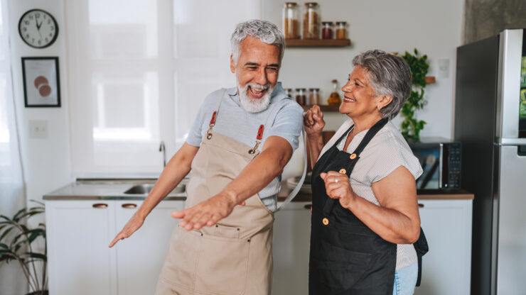 Senior couple wearing aprons joyfully dancing together in a bright, welcoming kitchen setting