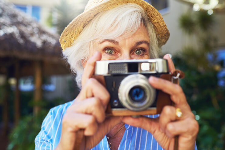 Senior woman enjoying outdoor moments, capturing memories with a vintage camera.