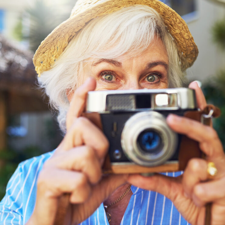 Senior woman enjoying outdoor moments, capturing memories with a vintage camera.