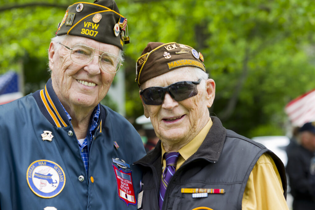 Two smiling veterans in uniform stand outdoors, sharing a moment of friendship and pride.