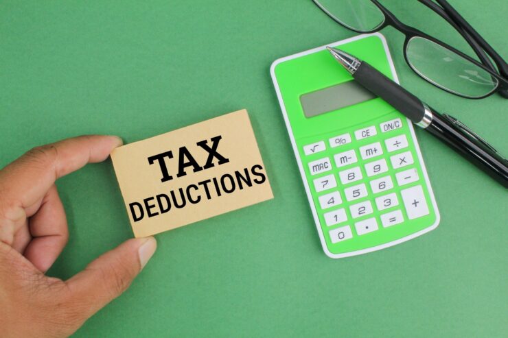 Hand holding a card labeled Tax Deductions beside a calculator, pen, and glasses on green table.