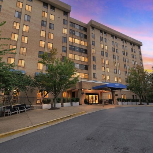 Well-lit retirement home exterior at sunset with welcoming entrance and green landscaping.