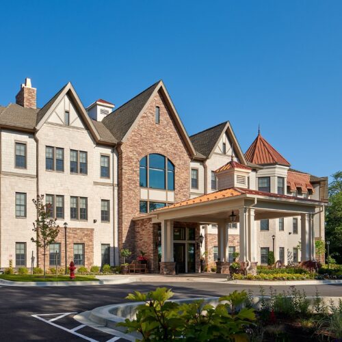 Elegant retirement community building with inviting entrance and well-maintained landscaping under clear skies.